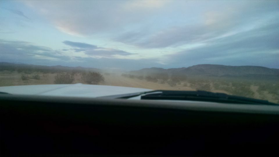 View from inside a vehicle driving on a dirt road in a desert landscape.
