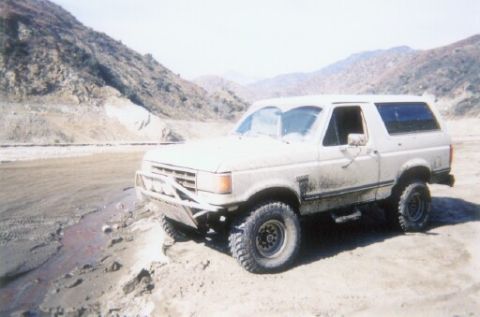 1988 Ford Bronco - A white Ford Bronco is parked on a dirt road in a mountainous area.