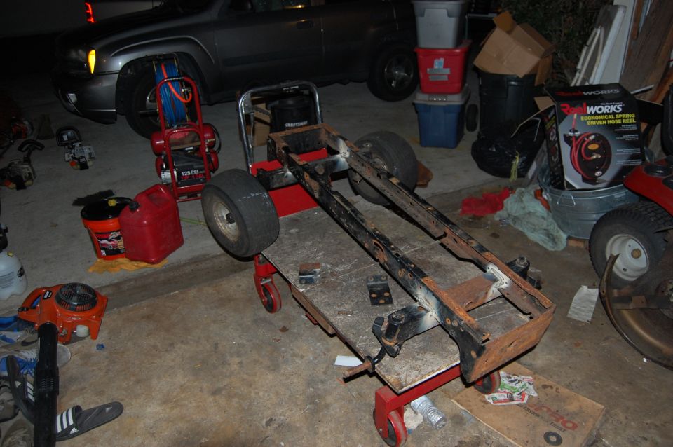Rusty vehicle frame on a creeper cart with tools.
