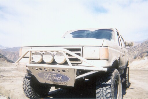 Tan lifted Ford Bronco with brush guard and off-road lights in desert