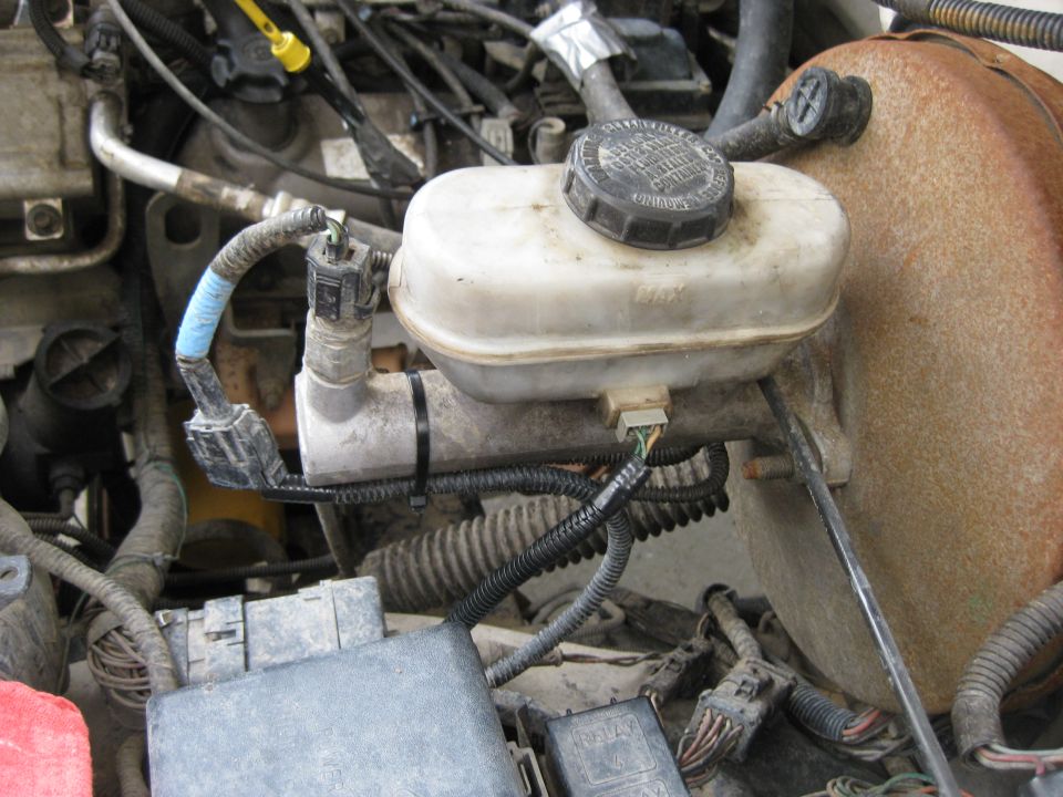 Engine bay view of brake fluid reservoir and master cylinder assembly with wiring.