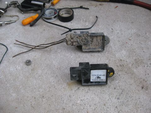 1994 Ford Bronco - Two automotive sensors are shown on a concrete surface. The top sensor is dirty and has wires extending from it. The bottom sensor has a la…