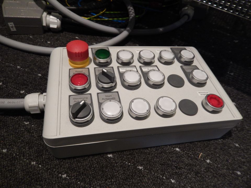 Gray control panel with red mushroom button, green button, red button, and multiple rotary switches.