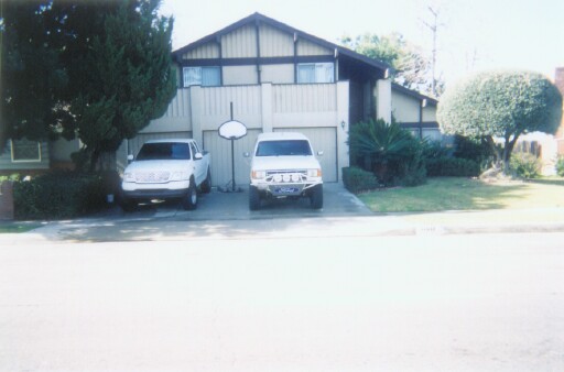 White lifted SUV with brush guard parked in driveway beside another white vehicle in front of a house
