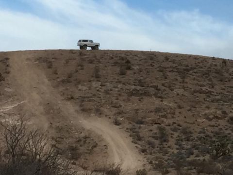 1979 Ford Bronco - An off-road vehicle navigates a dusty incline on a clear day.