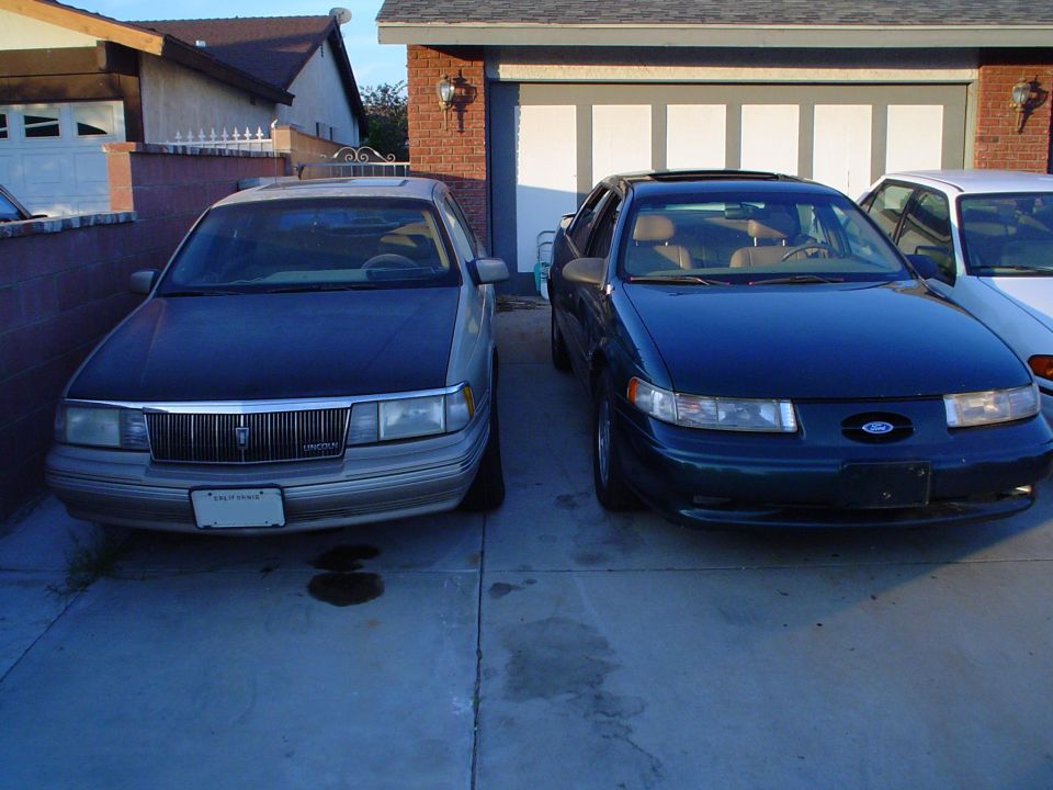 Tan Lincoln sedan and dark green Ford Taurus parked side by side in a driveway