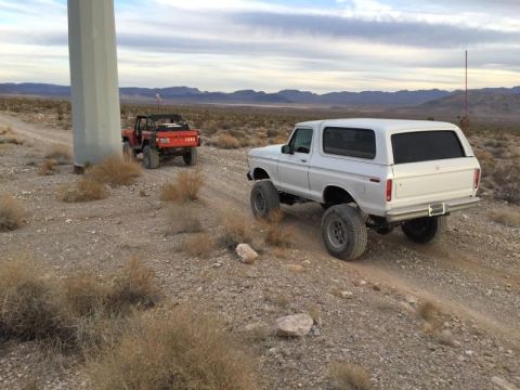 1979 Ford Bronco - Two SUVs, a white Bronco and a red truck, travel on a dusty desert road.