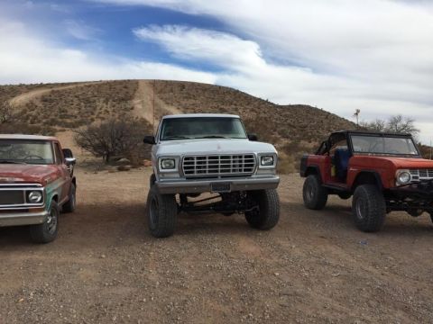 1979 Ford Bronco - Three SUVs are parked in an outdoor, dusty area with hills in the background under a cloudy sky.