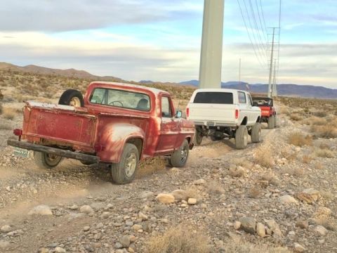 1979 Ford Bronco - Two trucks are parked in a dusty, outdoor area with a large pole in the background.
