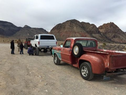 1979 Ford Bronco - A lifted 1979 Ford Bronco is being serviced by a group of people, with a vintage red pickup truck nearby.