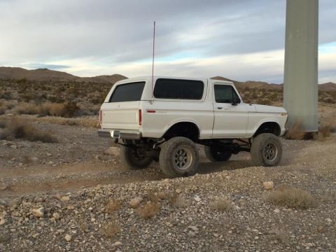 1979 Ford Bronco - White Ford Bronco with lifted suspension parked on a dirt road in a desert landscape.