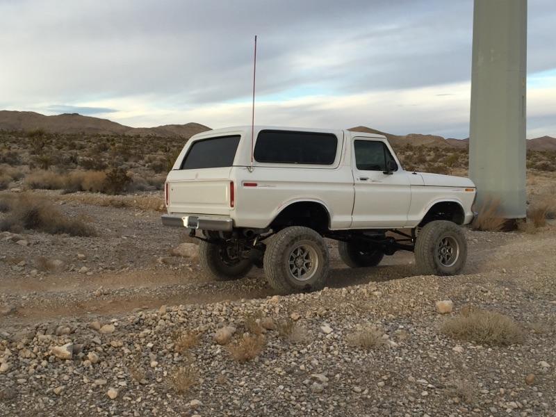 White Ford Bronco with lifted suspension parked on a dirt road in a desert landscape