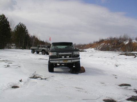 1979 Ford Bronco II - Two trucks are parked in a snowy, outdoor area. The front truck is black with a lifted suspension.