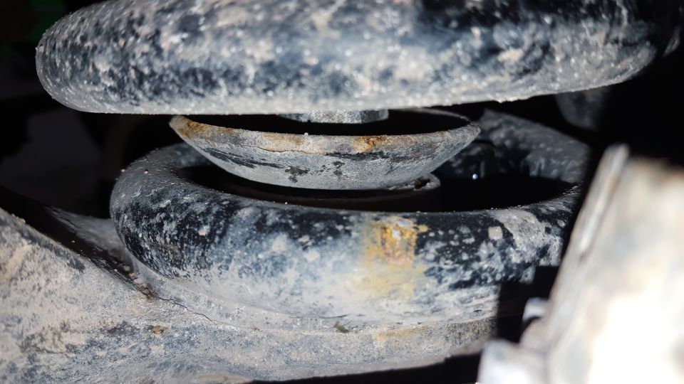 Close-up of a vehicle's suspension spring and mount with rust