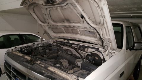 1995 Ford Bronco - Engine bay of a 1995 Ford Bronco, with another vehicle partially visible on the left.