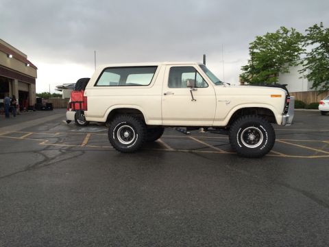 1981 Ford Bronco - A white 1981 Ford Bronco, equipped with off-road tires, is parked in a lot under a cloudy sky.