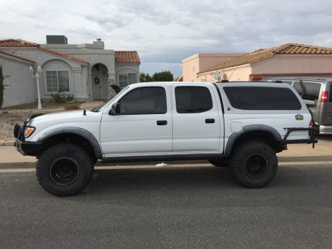 2001 Toyota Tacoma - This white 2001 Toyota Tacoma pickup truck features a camper shell and is equipped with off-road tires and suspension.