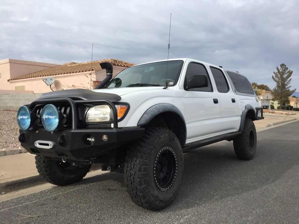 White 2001 Toyota Tacoma with aftermarket bumper, winch, PIAA lights, snorkel, and cap