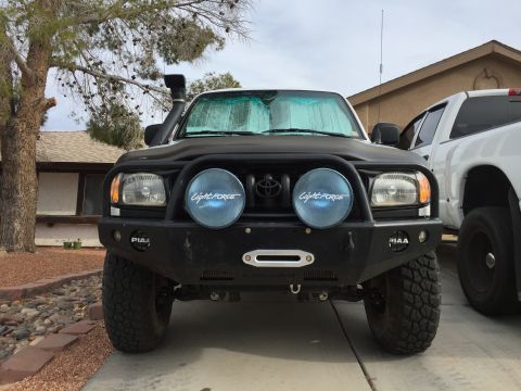 2001 Toyota Tacoma - Front view of a black 2001 Toyota Tacoma with aftermarket bumper and lights, parked next to a white truck.