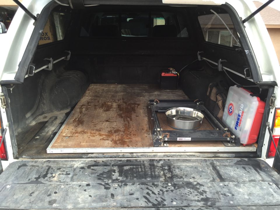 Truck bed with a wooden platform, a dog bowl on a sliding mechanism, a battery, and a first aid kit