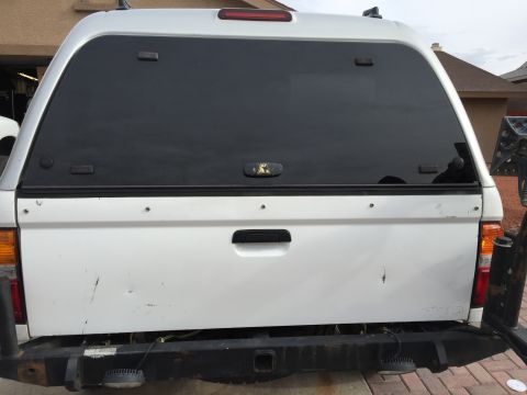 2001 Toyota Tacoma - The rear of a white pickup truck is shown, fitted with a black camper shell and a heavy-duty aftermarket bumper.