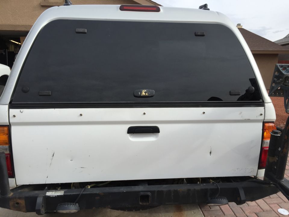 Rear view of white pickup truck with black camper shell and aftermarket bumper