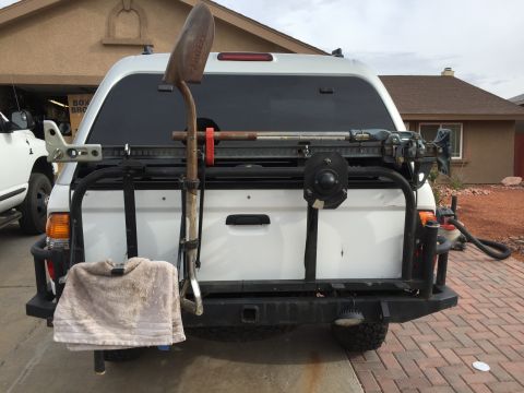 2001 Toyota Tacoma - This white pickup truck features a rear rack with a shovel and hi-lift jack, along with a towel hanging from the bumper.