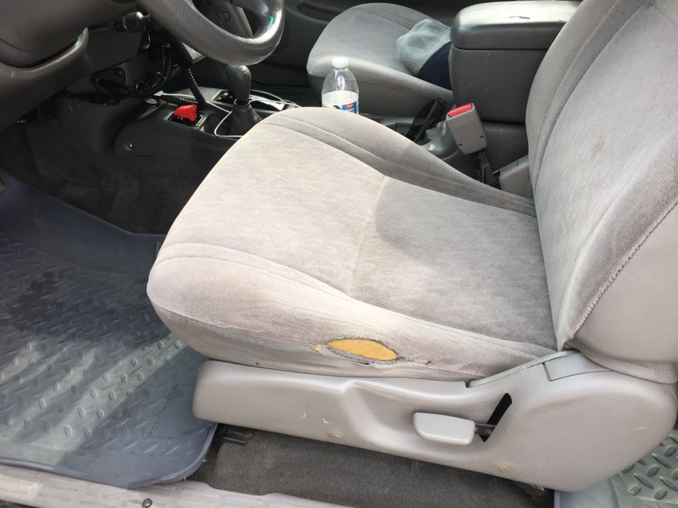 Torn fabric on driver's seat of a vehicle, showing exposed yellow padding