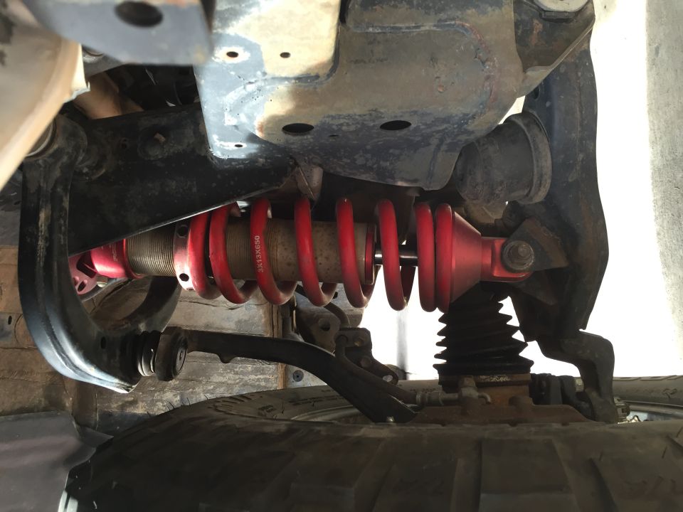 Underside view of a red coilover shock absorber with visible text, attached to vehicle suspension components and a tire