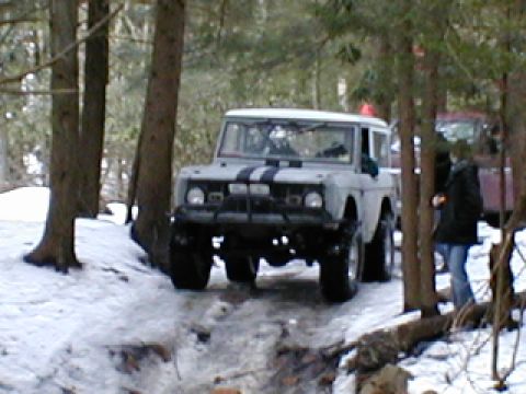 1979 Ford Bronco II - A light-colored SUV with racing stripes navigates a snowy path, with another vehicle and a person visible in the background.