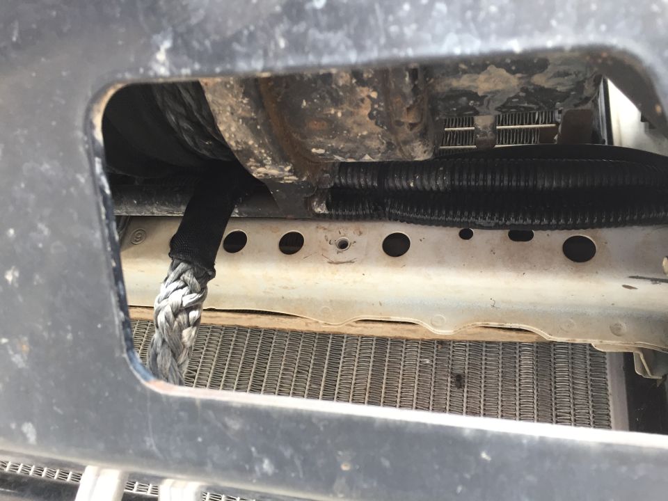 Winch cable emerging from a black housing, with a radiator visible behind a metal frame