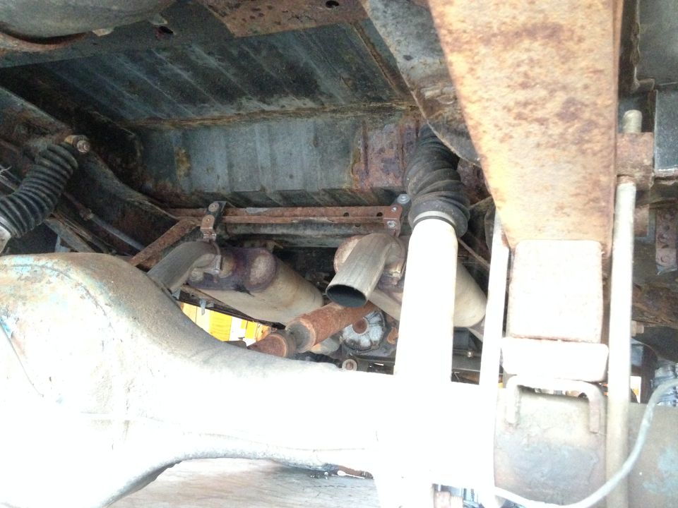 Underside of a vehicle showing the rear axle, exhaust pipes, and suspension components. Lots of rust visible