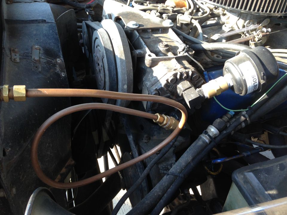 Engine bay showing AC compressor, hoses, and a pressure gauge attached