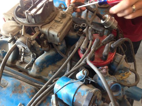 1979 Ford Bronco - Close-up view of an engine bay, focusing on the carburetor and distributor assembly, with hands performing maintenance.