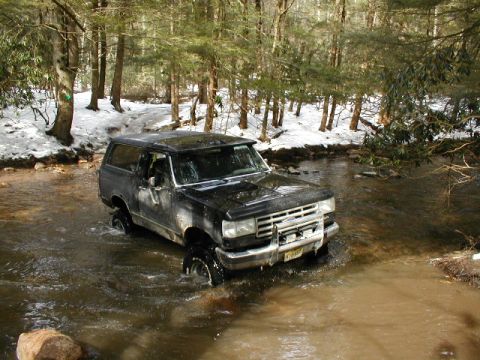 1979 Ford Bronco II - A black Ford Bronco navigates a stream in a snowy, wooded environment.