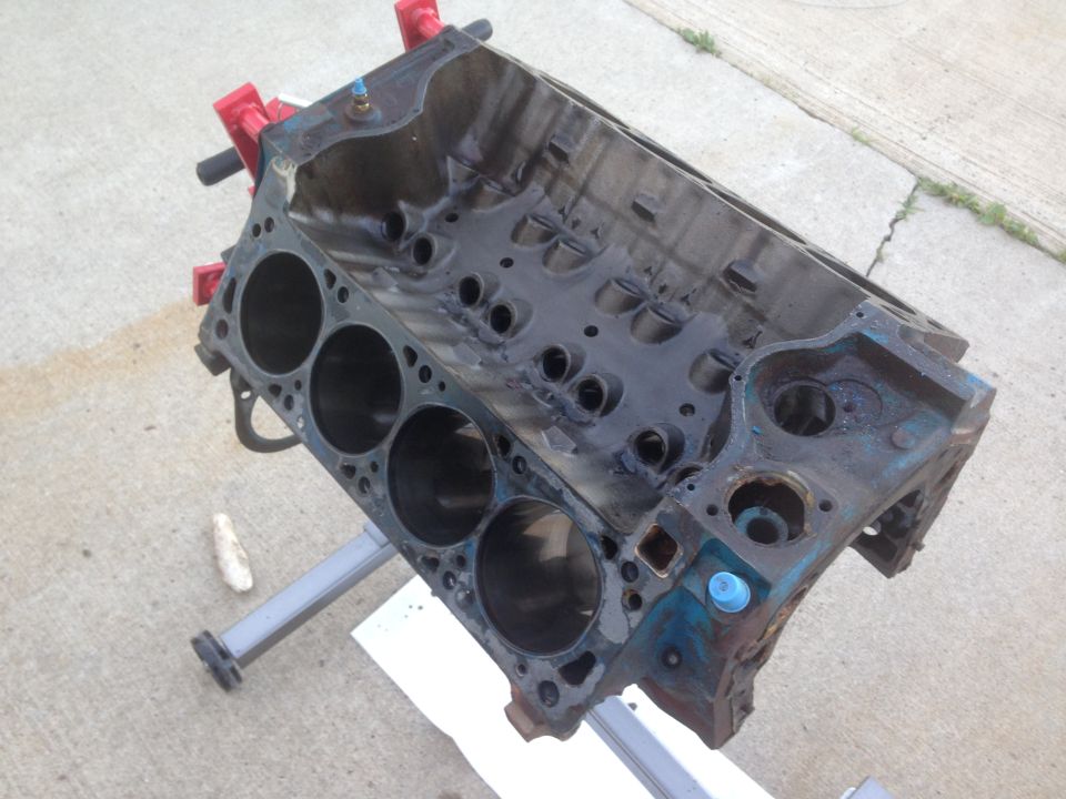 Engine block on a stand, showing cylinder bores and internal passages. Some blue paint is visible
