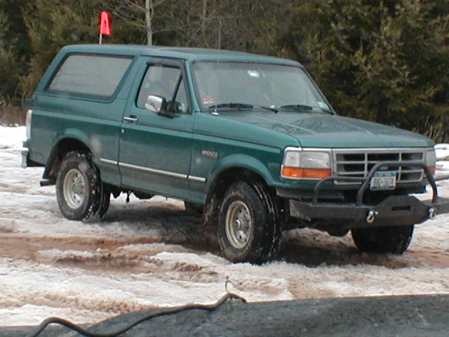 Green 1990s Ford Bronco with black winch bumper and brush guard parked in snow and mud