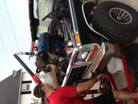 1979 Ford Bronco - Mechanic works on removing the engine from a black 1978 Ford Bronco using an engine hoist.
