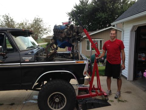 1979 Ford Bronco - A black 1979 Ford Bronco is shown with its engine being removed using an engine hoist, with a man standing nearby.