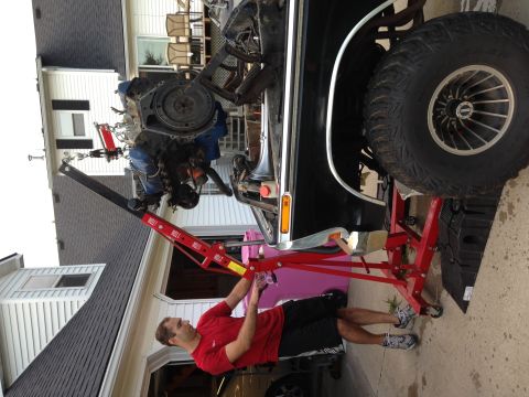 1979 Ford Bronco - A person is using an engine hoist to remove the engine from a black SUV in a driveway.
