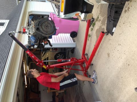 1979 Ford Bronco - An engine is being lifted out of a vehicle using a red engine hoist in a garage setting.