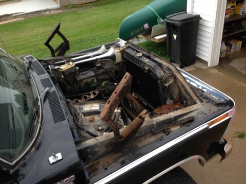 1979 Ford Bronco - The engine bay of a black vehicle is exposed, revealing engine parts and a pair of large air horns mounted above the radiator.