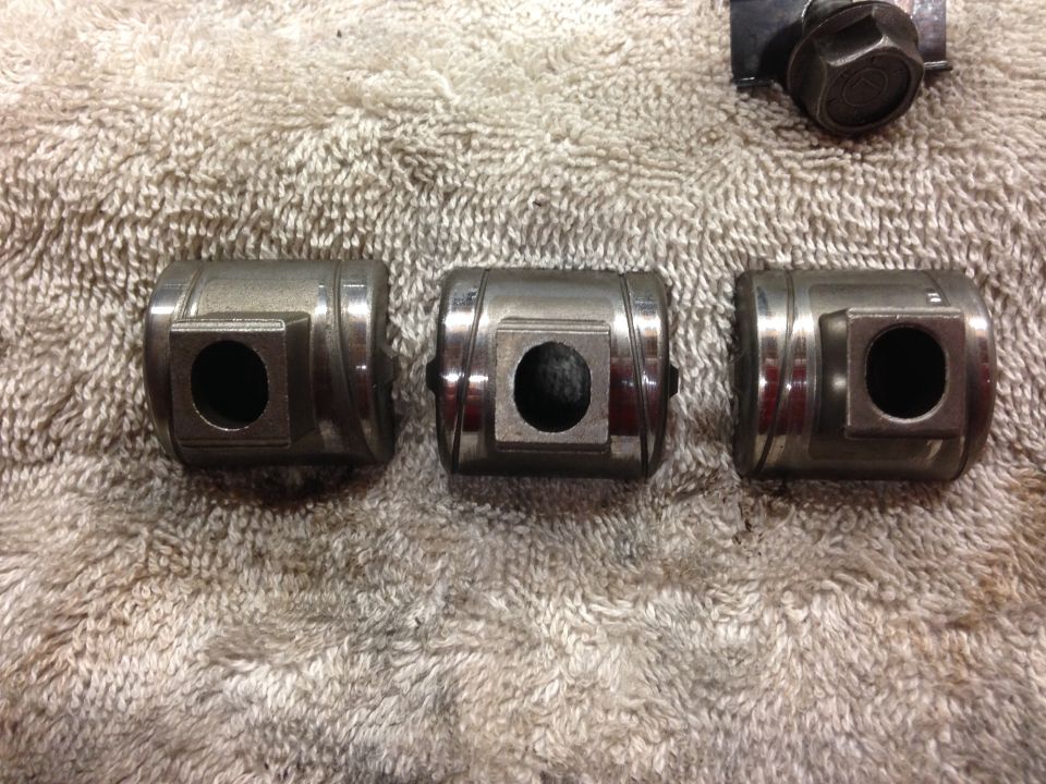Three metal engine valve lifters on a towel. A bolt is visible in the upper right