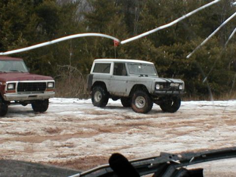 1979 Ford Bronco II - Two off-road vehicles, including a gray Ford Bronco, are parked on a dirt road covered in snow and mud.