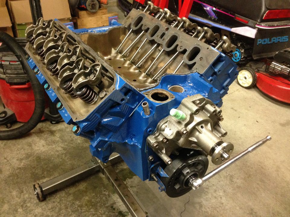 Blue V8 engine block with valve covers removed, on an engine stand. Water pump assembly attached