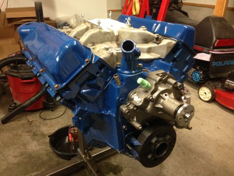 1979 Ford Bronco - Engine assembly painted blue, mounted on a stand with a water pump attached. Other equipment is visible in the background.