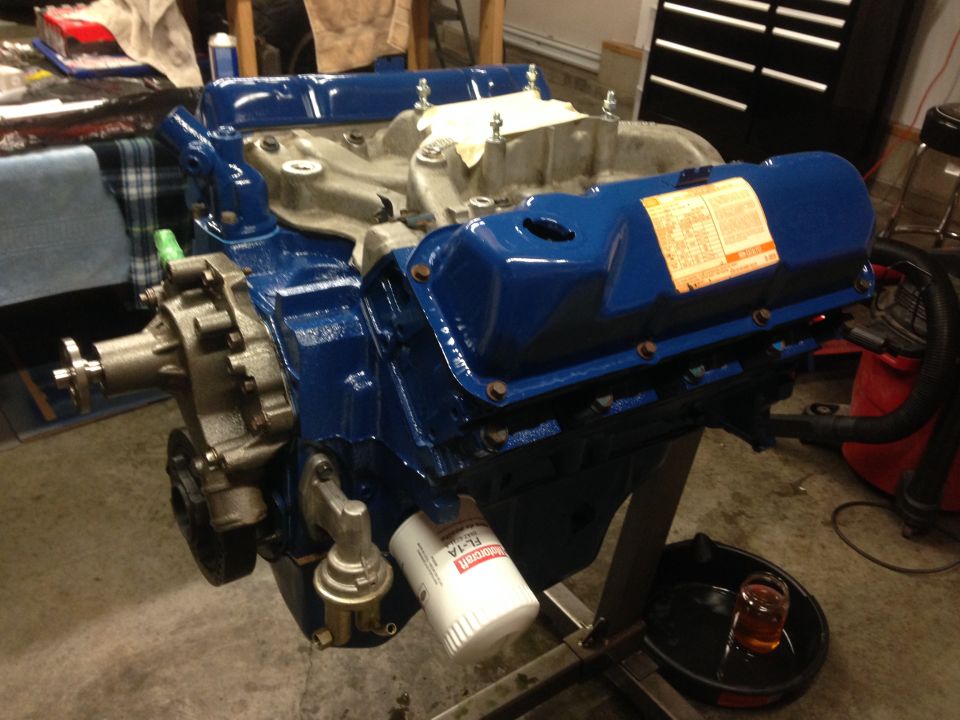 Blue V8 engine on stand with oil filter and fuel pump. Label on valve cover is visible