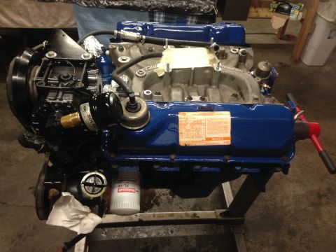 1979 Ford Bronco - Engine rebuild with a blue Ford V8 motor on a stand, an oil filter and various hoses.