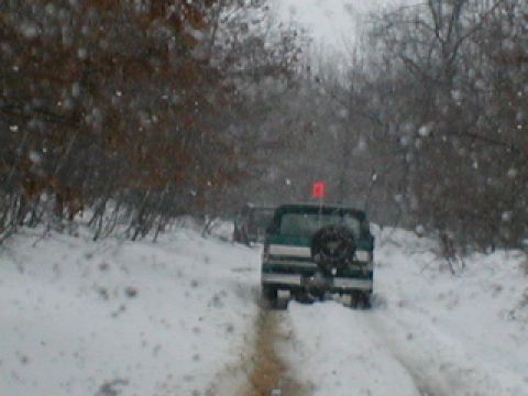 1979 Ford Bronco II - Two SUVs navigate a snowy path through a wooded area during winter weather.
