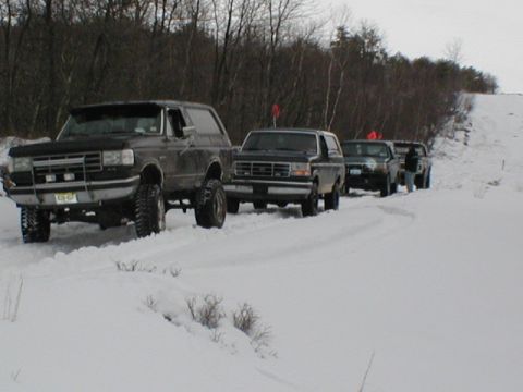 1979 Ford Bronco II - A line of Ford Broncos navigate a snowy trail, with the lead vehicle a prominent brush guard.
